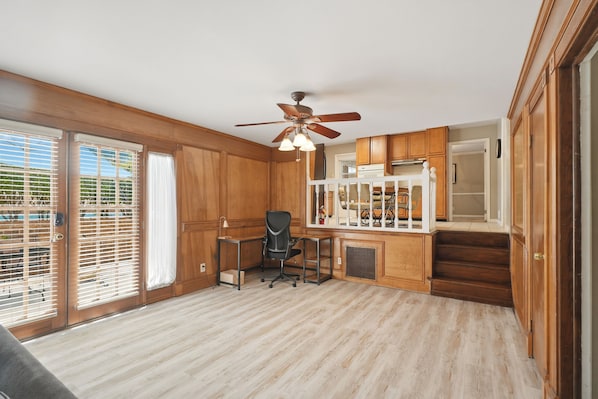 A room with wooden paneling, a ceiling fan, a desk with a chair, and a view through large windows. - Private Pool, Patio! Spacious Home in Decatur (Decatur)