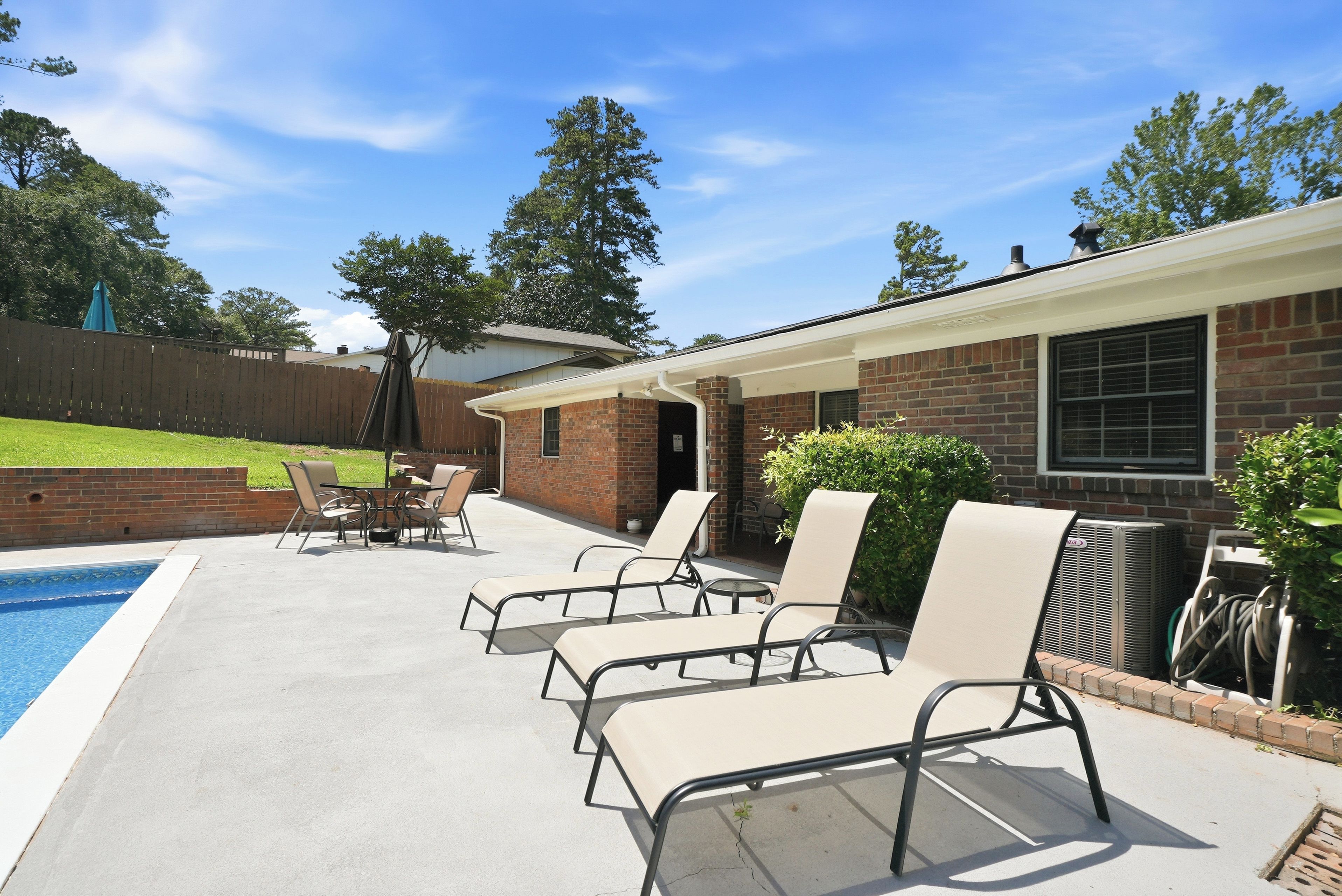 A backyard with a swimming pool, lounge chairs, and a brick house.