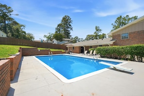 A rectangular swimming pool with a brick border, surrounded by a concrete deck.