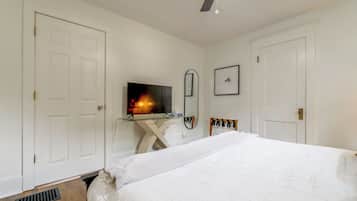 Ein Schlafzimmer mit einem Bett, einem Fernseher auf einem Glastisch, einem Deckenventilator und weißen Wänden.