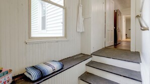 Una escalera que lleva a una puerta, una ventana con persianas, y un tapete enrollado en el suelo.