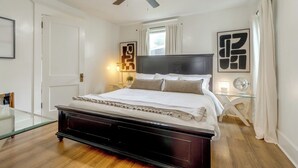 Un dormitorio con una cama de madera oscura, un ventilador de techo, una mesita de noche con una lámpara y obras de arte en las paredes.