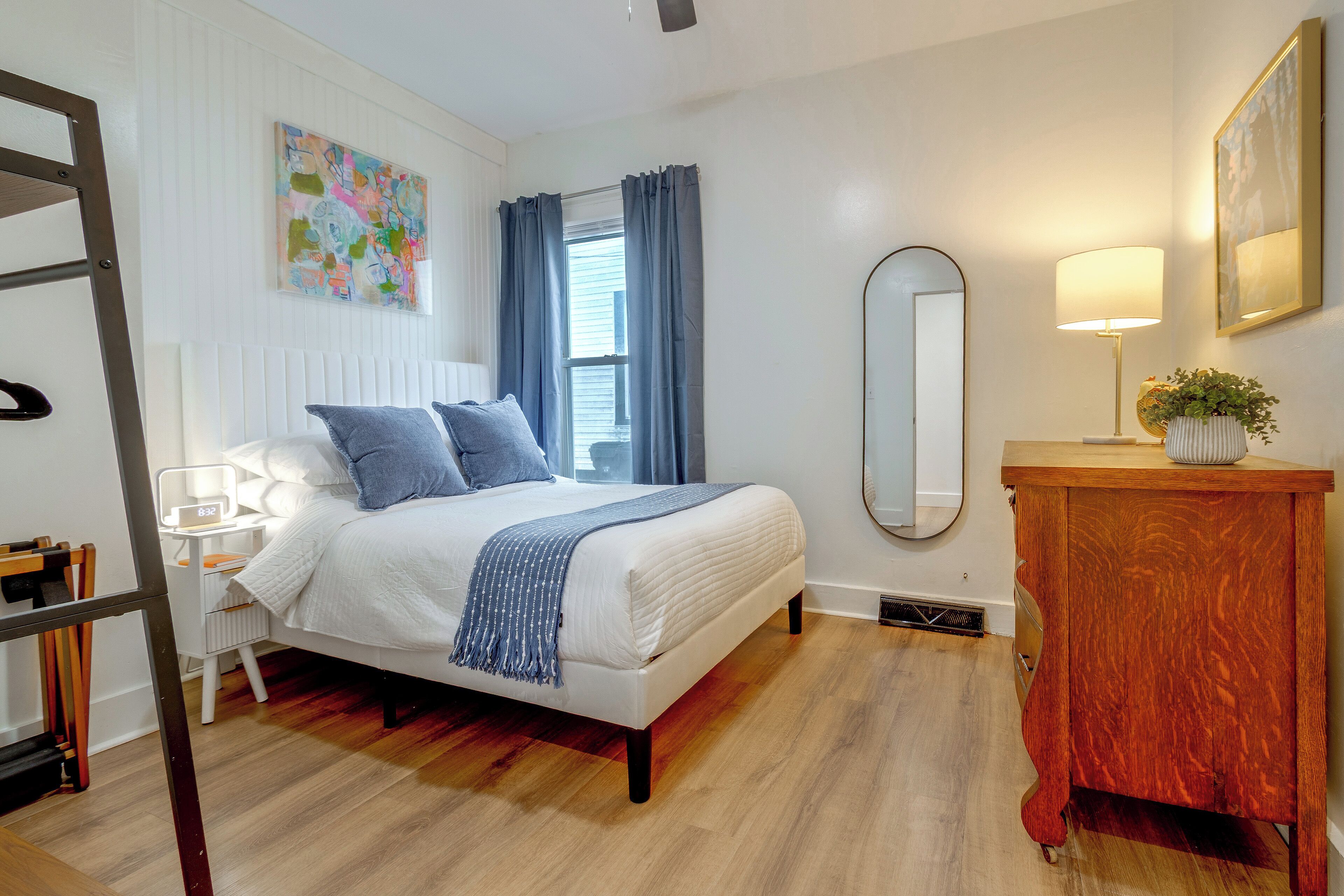 A bedroom with a bed, a dresser, a mirror, and a window with curtains.
