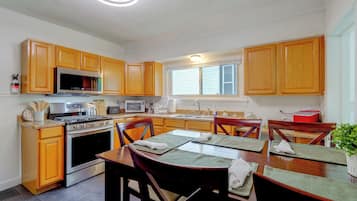 A kitchen with wooden cabinets, stainless steel appliances, a dining table with chairs, and a window with blinds.