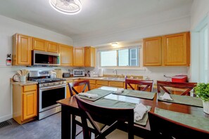 A kitchen with wooden cabinets, stainless steel appliances, a dining table with chairs, and a window with blinds. - Cozy 3-bedroom Home Close to ISU & Iwu, Sleeps 6 (Bloomington)