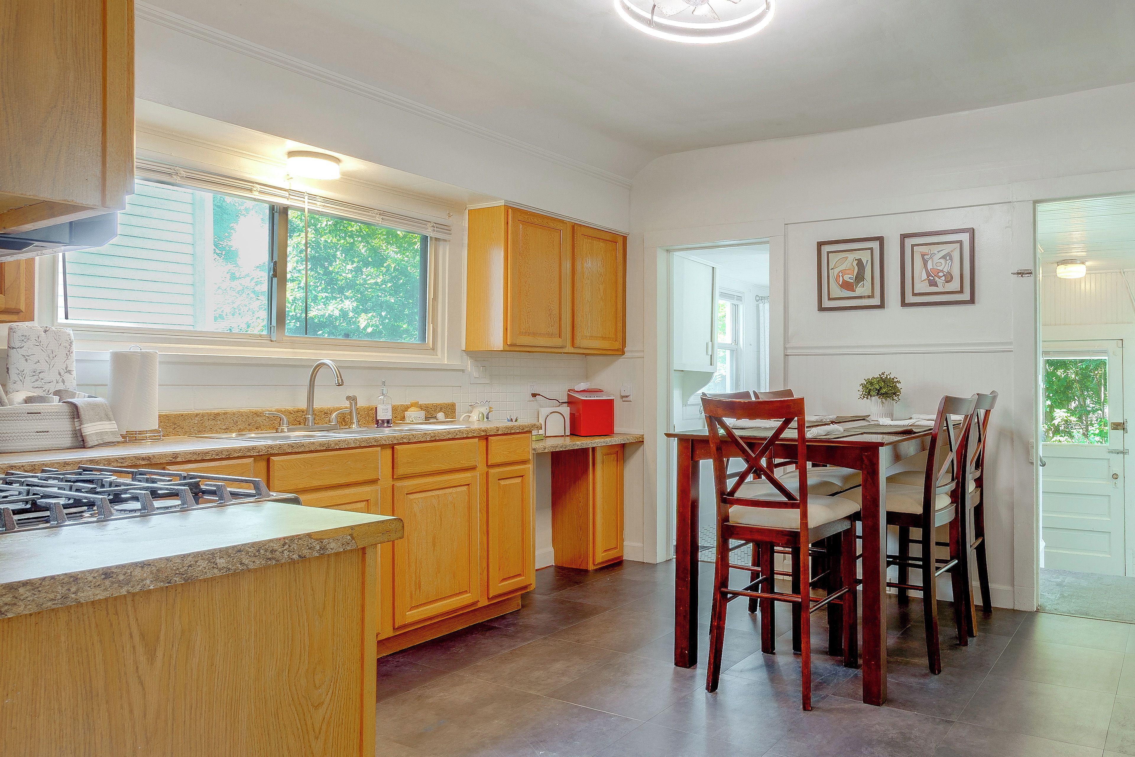 A kitchen with wooden cabinets, a gas stove, and a dining area with chairs and a table.
