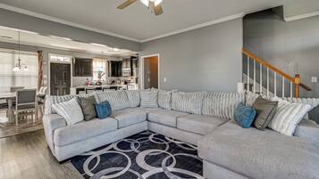 A modern living room with a sectional sofa, a patterned rug, and a ceiling fan.