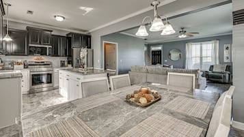 A modern kitchen with dark cabinets, a dining area with a marble table, and a living room with a gray sofa.