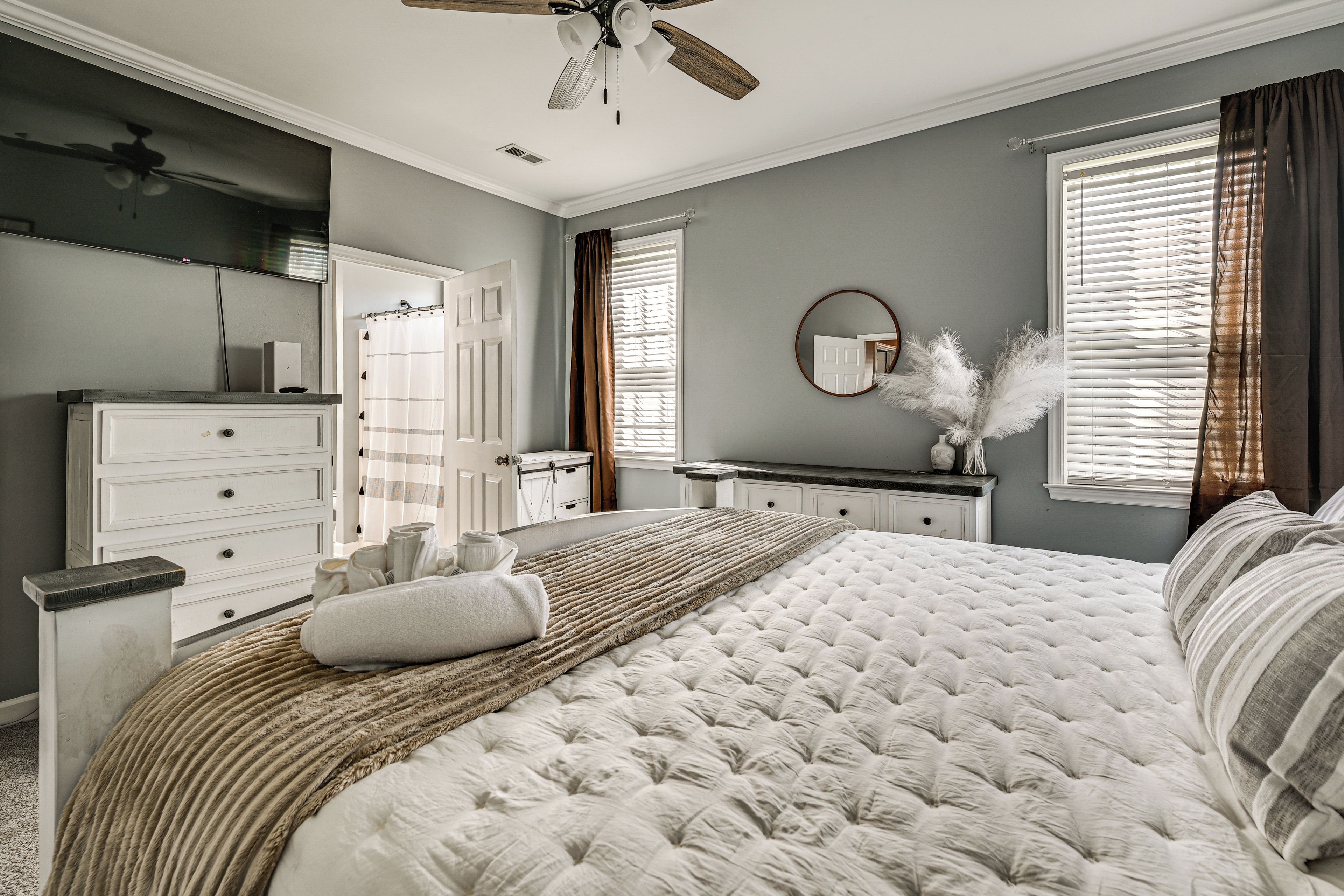 Une chambre à coucher avec un grand lit, une commode, une coiffeuse et un ventilateur de plafond.