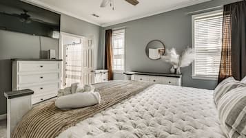 A bedroom with a large bed, a dresser, a vanity, and a ceiling fan.