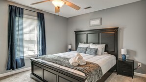 Ein Schlafzimmer mit einem dunklen Holzbett, einem Deckenventilator, einem Fenster mit Jalousien und einem Nachttisch mit Lampe.