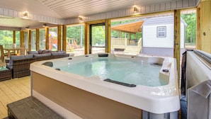 Uma banheira de hidromassagem em área externa coberta, com deck de madeira e vista para uma casa.