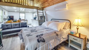 Um quarto com cama, mesa de cabeceira, escrivaninha, sofá e escada para um andar superior.