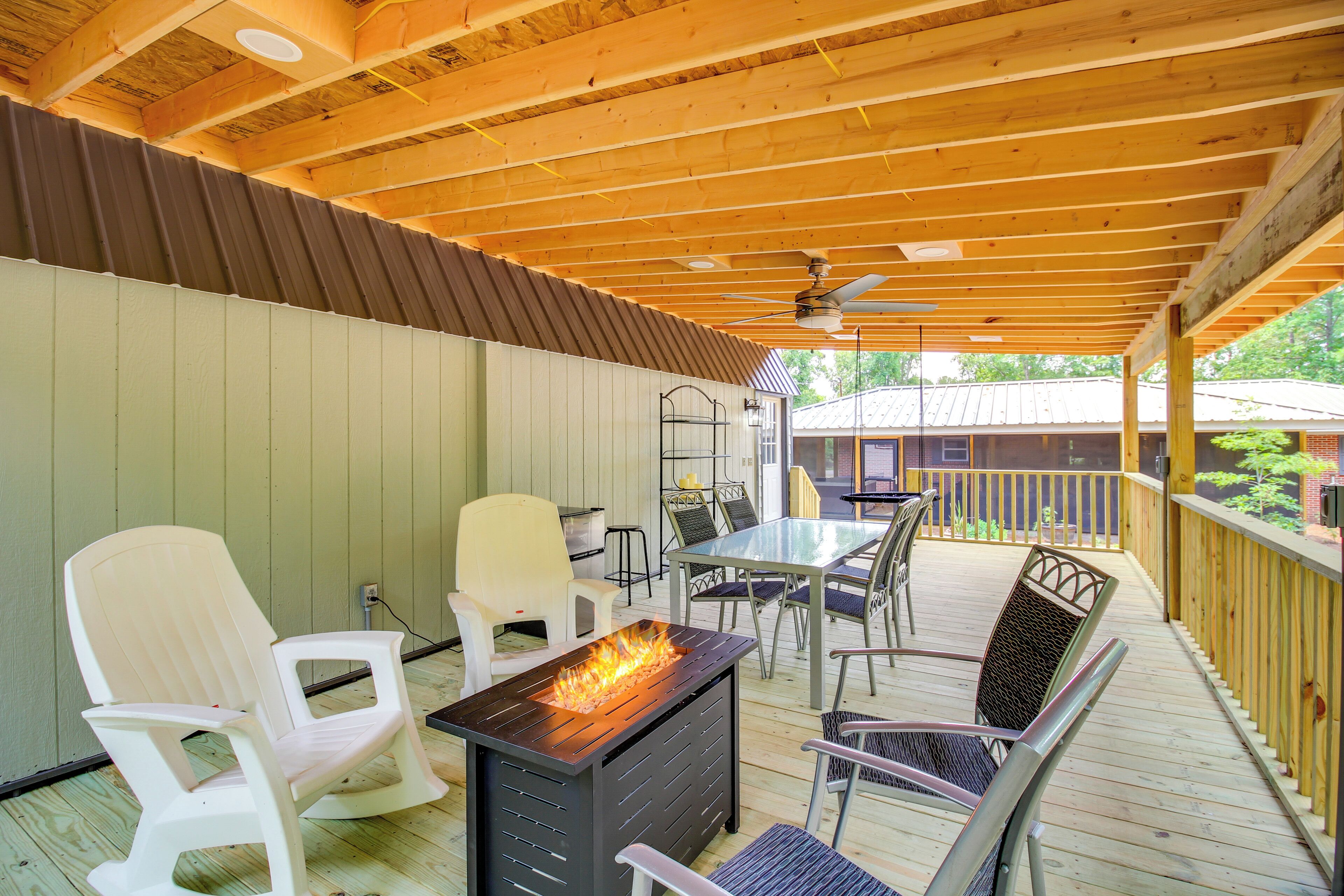Une terrasse extérieure couverte, dotée d’un foyer, de sièges et offrant une vue sur une maison en arrière-plan.