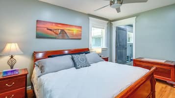A bedroom with a bed, nightstands, a ceiling fan, a painting, and a door leading to another room.
