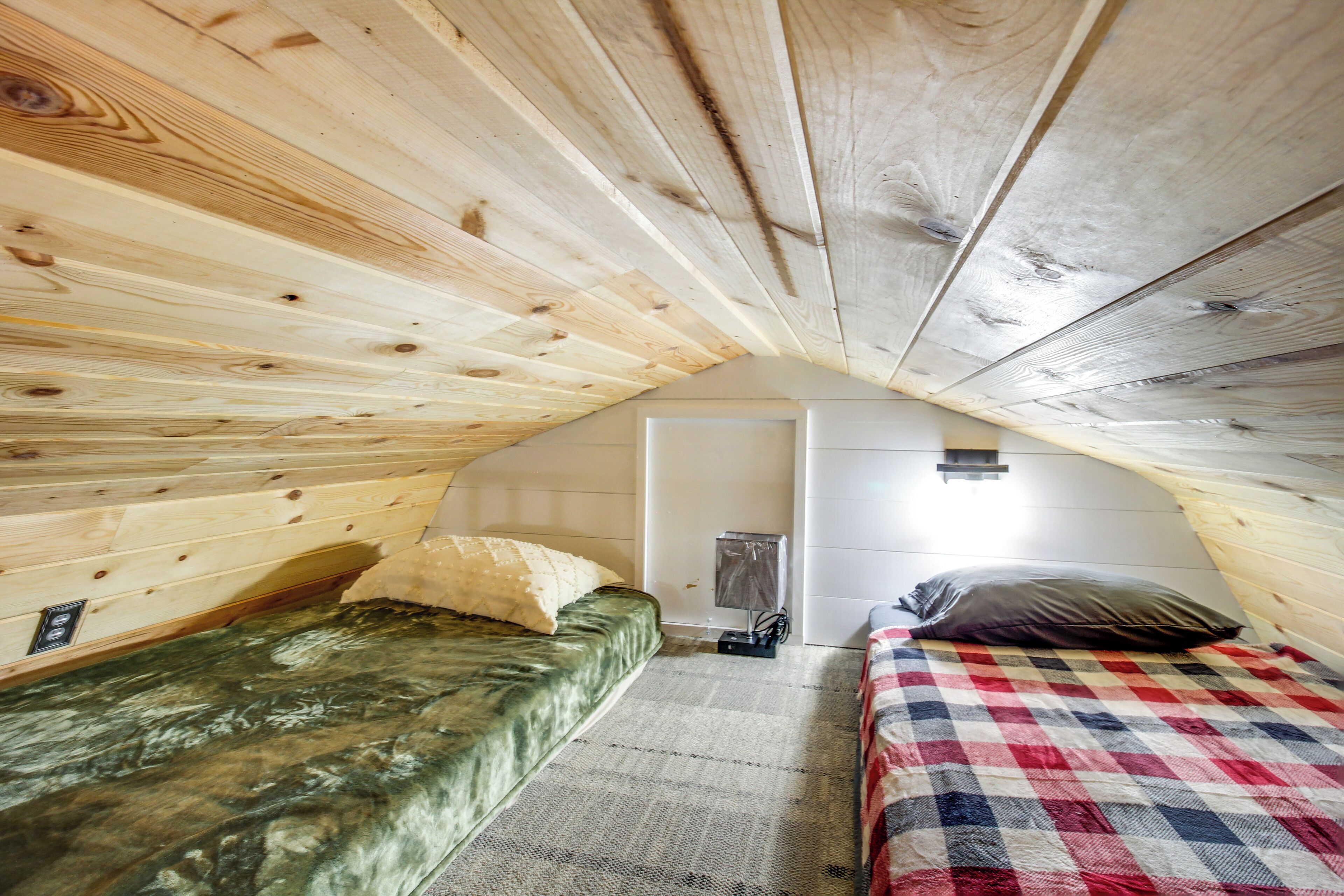 Une chambre confortable située dans les combles, avec des murs en bois, deux lits, une petite table et un luminaire.