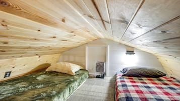 A cozy attic bedroom with wooden walls, two beds, a small table, and a light fixture.