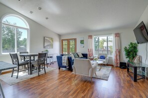 A spacious living room with hardwood flooring, a dining area with a table and chairs, a blue sofa, a white armchair, and a glass coffee table. - 5BR Home Close to Moorhead Home & Fargo (Moorhead)