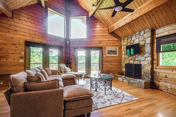 A log cabin interior with a sectional sofa, a fireplace, and a ceiling fan. - Pinnacle Lakefront Retreat: Dock, Canoe & Fire Pit (Pinnacle)