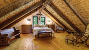 A cozy attic bedroom with a wooden floor, a bed, a bench, a dresser, and a rocking chair. - Lakefront Log Cabin w/ Views & Dock in Brandon (Brandon)