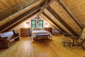 Ein gemütliches Schlafzimmer im Dachgeschoss mit Holzboden, einem Bett, einer Bank, einem Schminktisch und einem Schaukelstuhl.