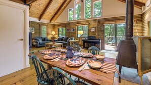 A log cabin interior with a dining area, sofas, a piano, and a wood stove. - Lakefront Log Cabin w/ Views & Dock in Brandon (Brandon)