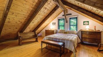 A cozy attic bedroom with a sloped ceiling, wooden floors, a bed with a quilt, two nightstands, a bench, and a dresser.