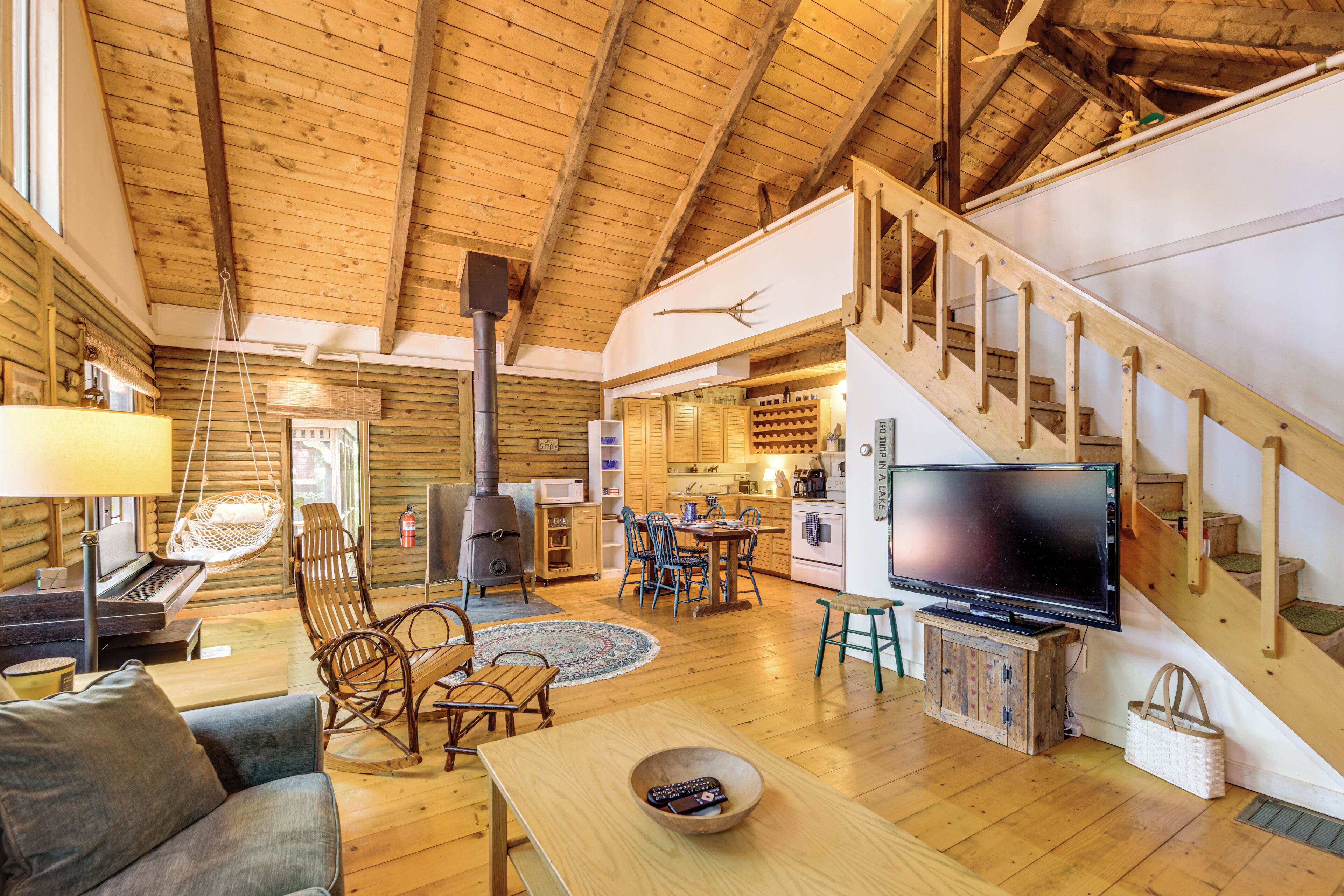A cozy cabin interior with a wooden floor, a sofa, a dining area, a kitchen, and a staircase.