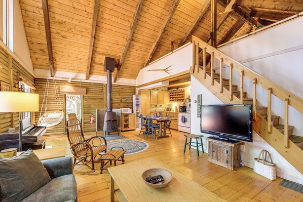 A cozy cabin interior with a wooden floor, a sofa, a dining area, a kitchen, and a staircase.