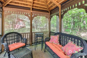 A covered outdoor seating area with wicker furniture and a view of the forest.