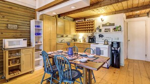 A compact kitchen with wooden cabinets, a dining table set for four, and a water dispenser. - Lakefront Log Cabin w/ Views & Dock in Brandon (Brandon)