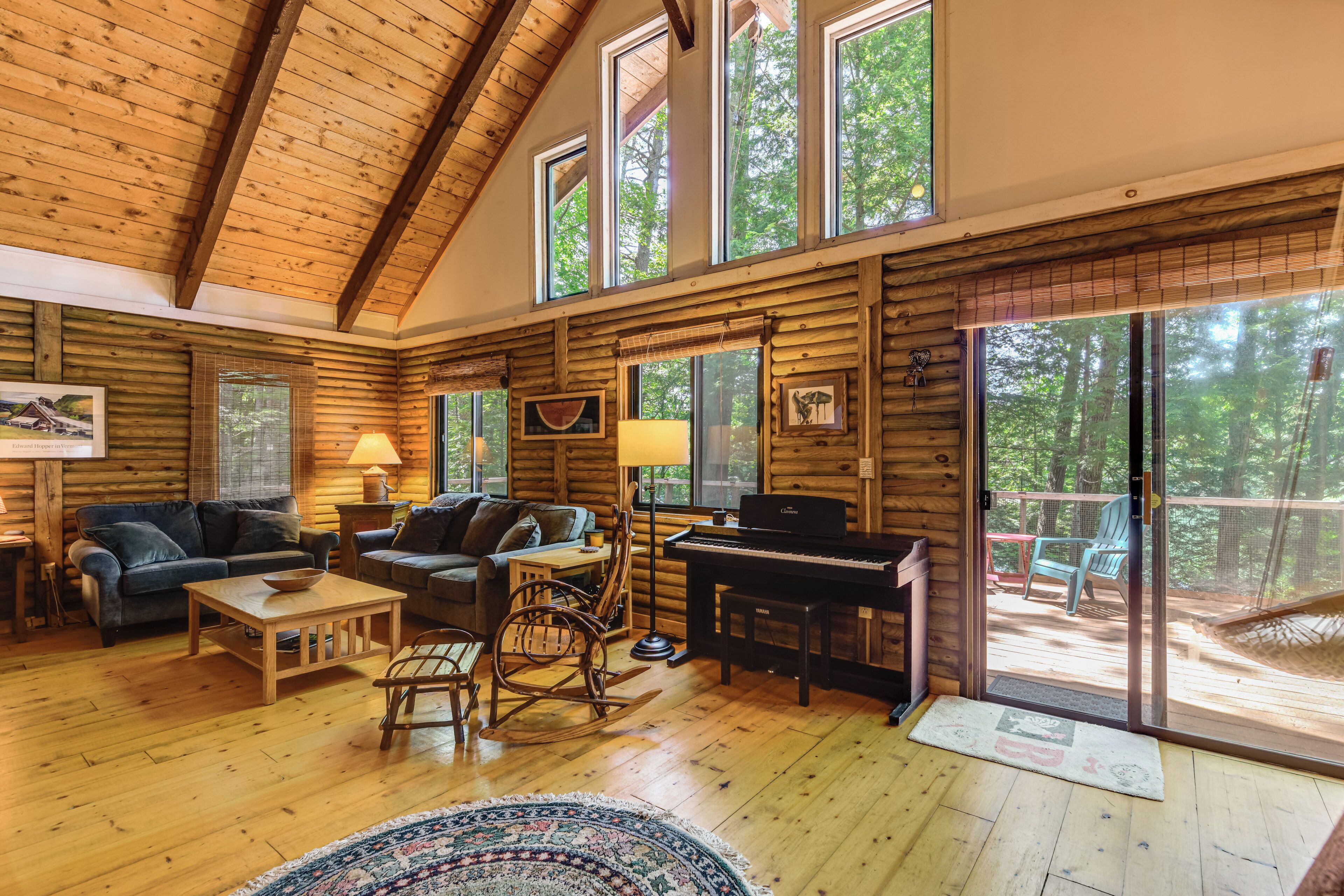 A log cabin interior with a piano, seating area, and large windows.