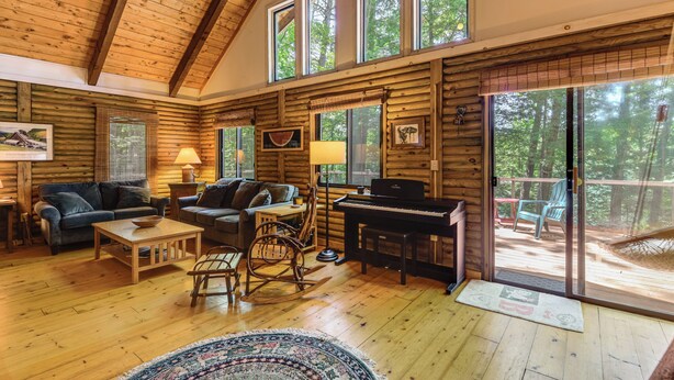 A log cabin interior with a piano, seating area, and large windows. - Lakefront Log Cabin w/ Views & Dock in Brandon (Brandon)
