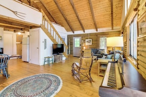 A spacious living area with a wooden floor, a television, a piano, and a cozy seating arrangement.