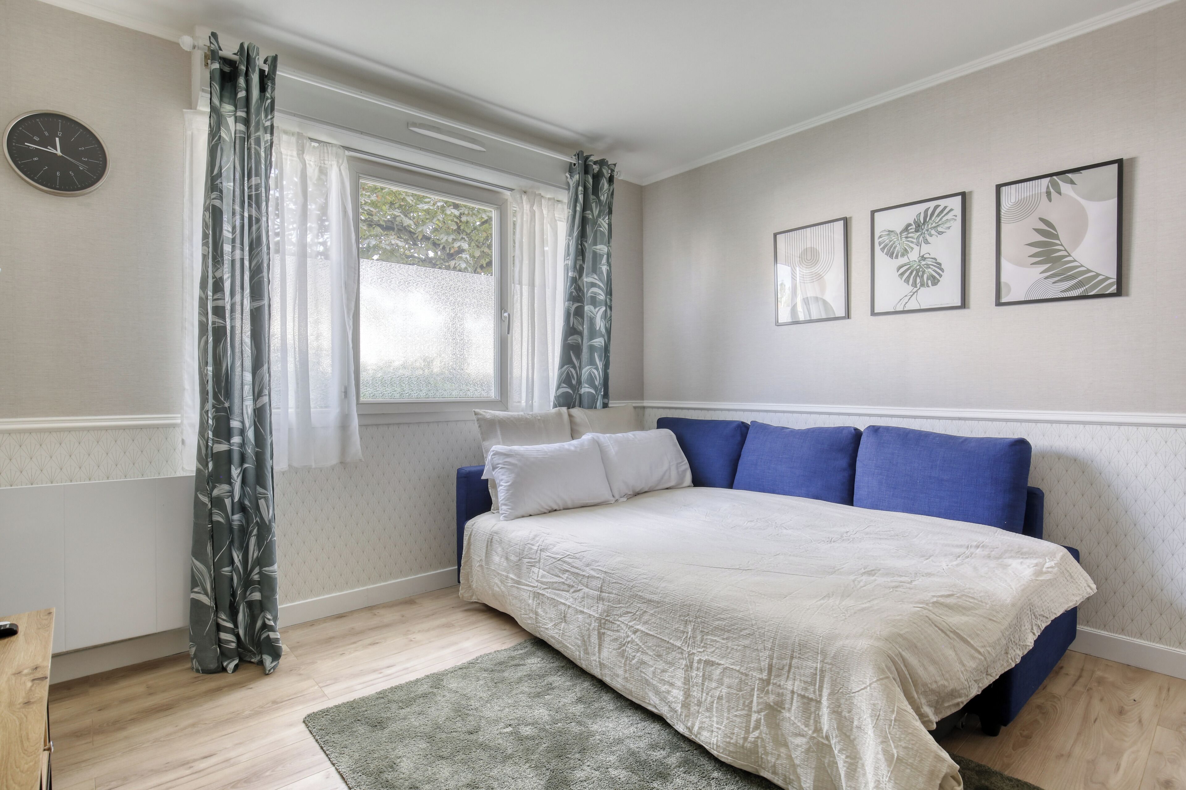 Une chambre à coucher avec un lit, des rideaux, une horloge et des œuvres d’art encadrées accrochées au mur.