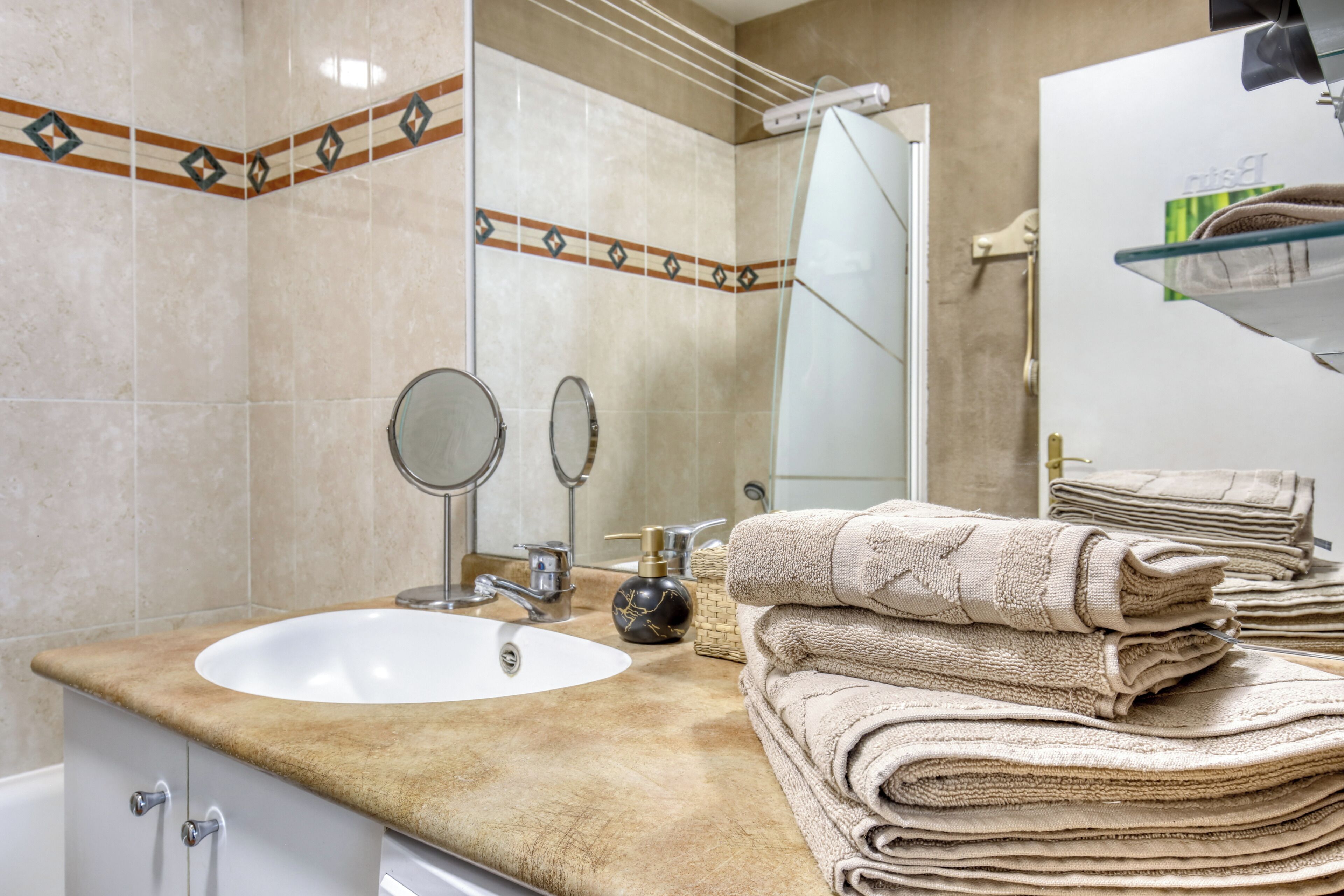 A bathroom with a sink, two mirrors, a towel stack, and a towel rack.