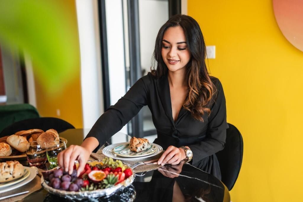 A person seated at a table with a variety of food items including bread, a salad, and a plate with a baked dish.