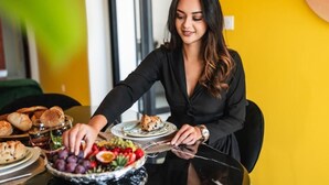 A person seated at a table with a variety of food items including bread, a salad, and a plate with a baked dish. - Takeoff (SAINTE-MARIE)