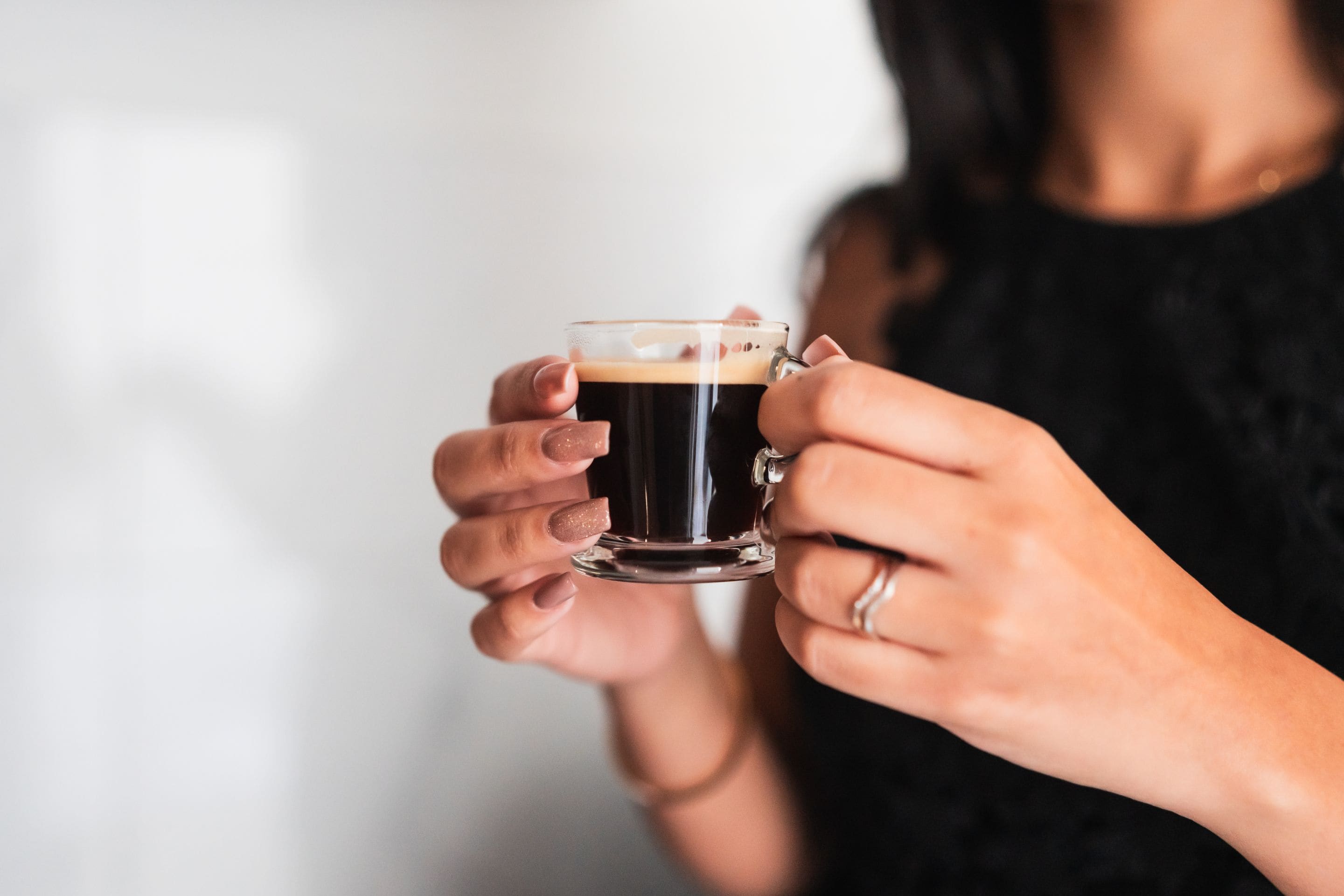 Une personne tenant une tasse en verre transparent contenant un liquide foncé, probablement du café ou du thé.