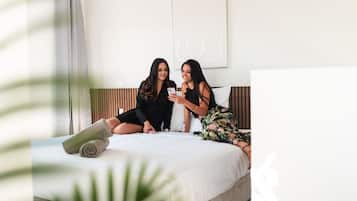 Deux femmes sont assises sur un lit dans une chambre d’hôtel, l’une d’elles tient un téléphone.