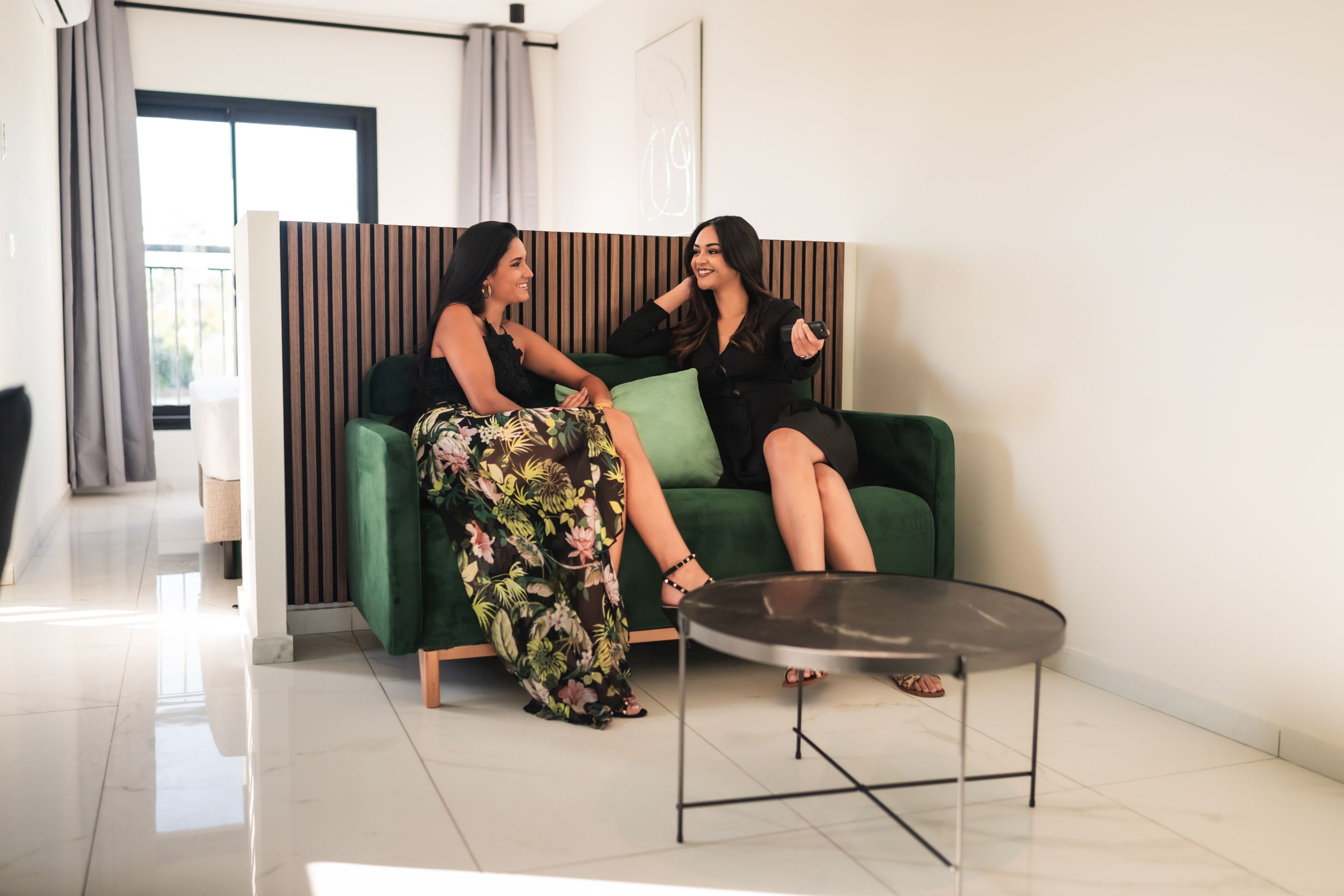 Deux personnes sont assises sur un canapé vert dans un intérieur moderne, devant une table basse en verre.