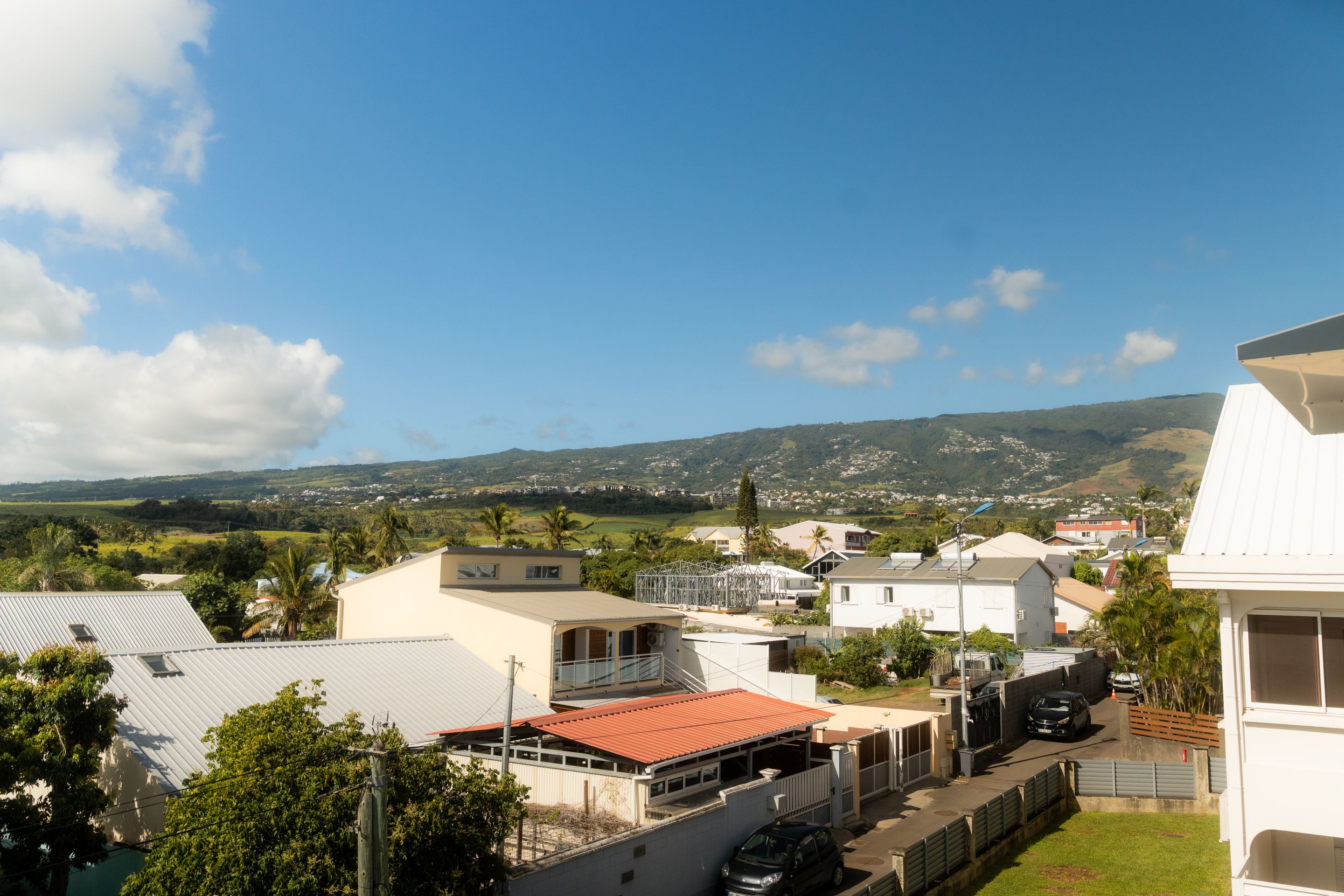 A residential area with houses, a street, and a hilly landscape in the background.