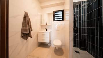 Um banheiro moderno com toucador branco, vaso sanitário e área de chuveiro com azulejos pretos.