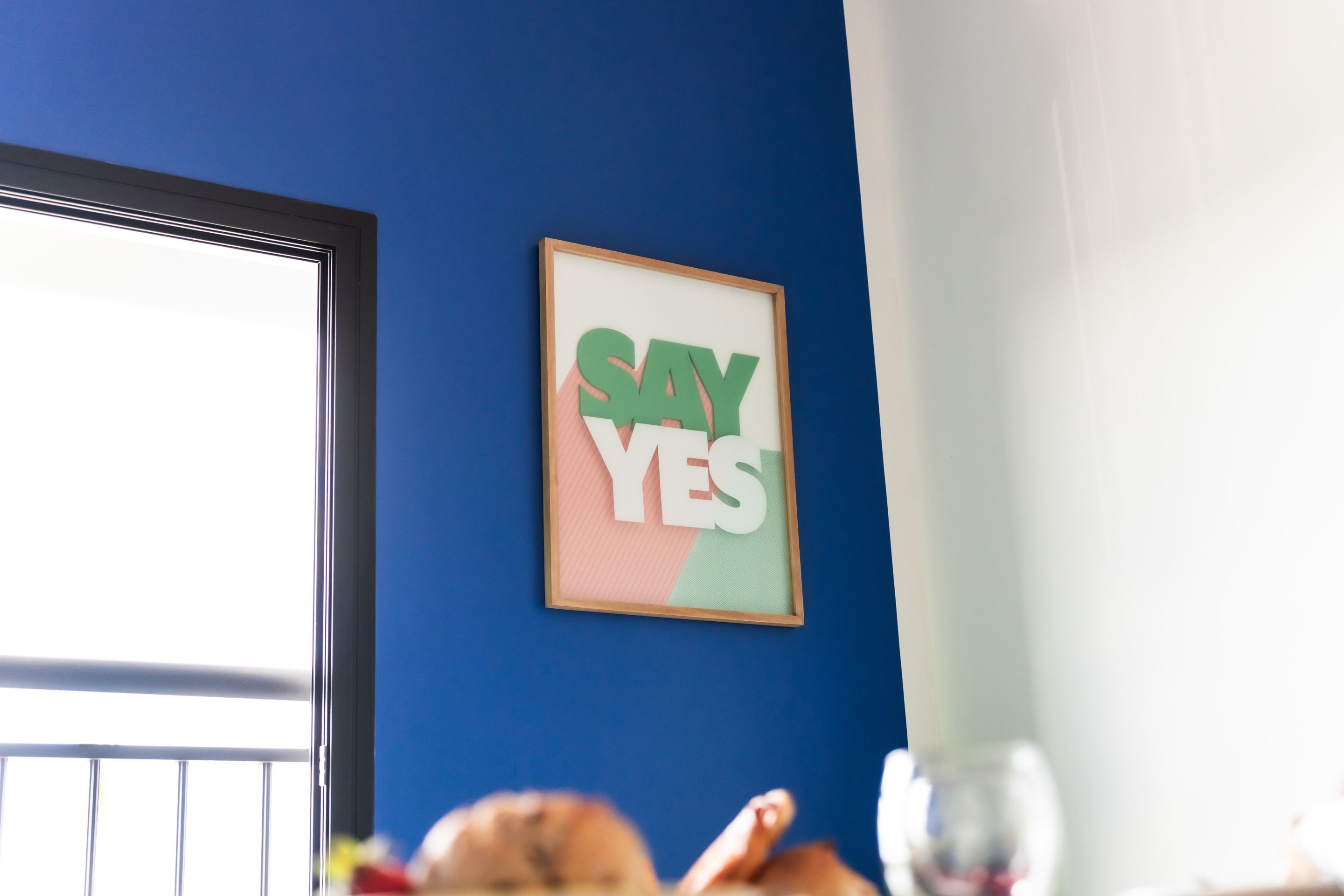 A framed sign with the words "SAY YES" on a blue wall.