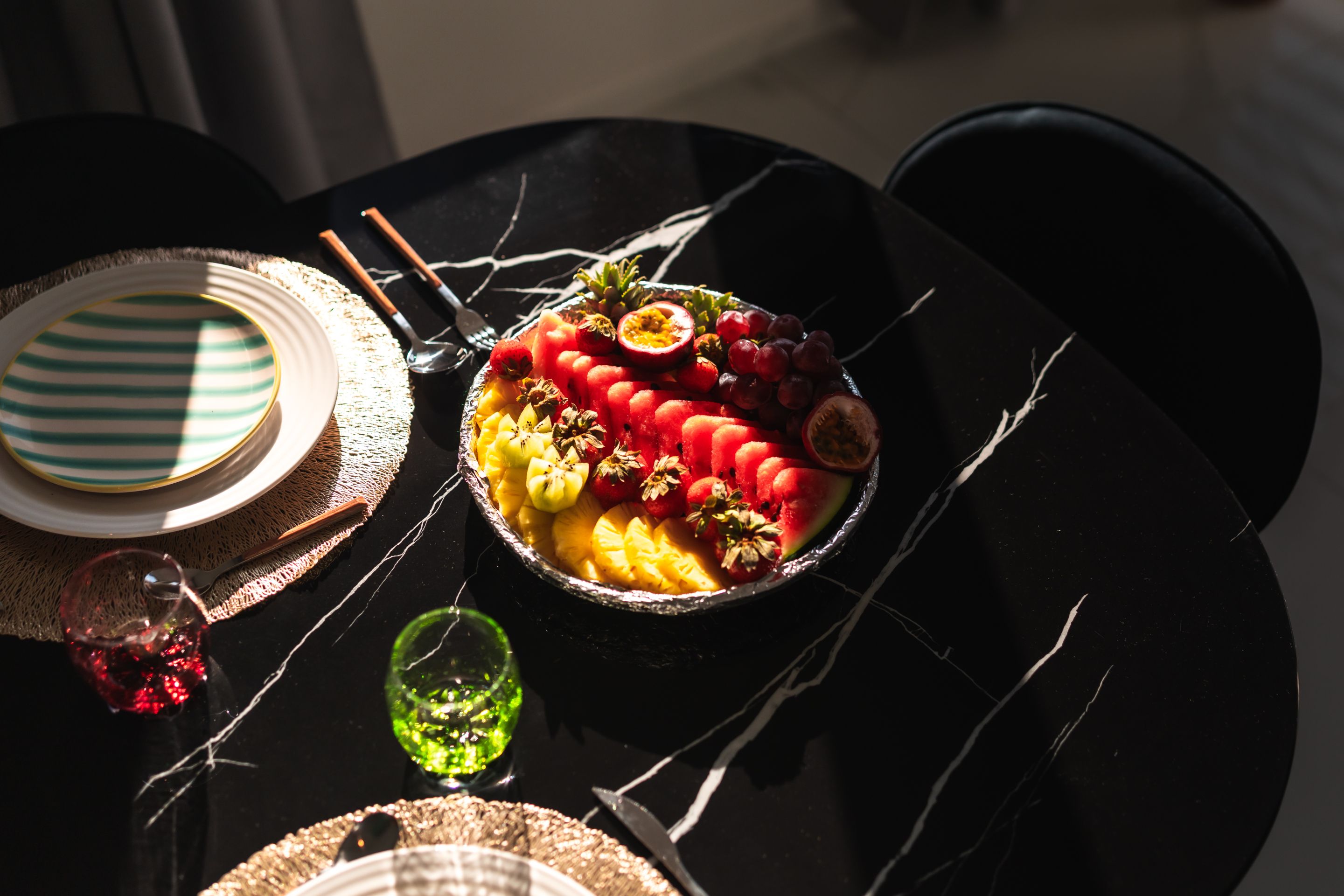 A table with a fruit bowl, striped plates, and chopsticks.