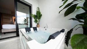 A modern bathroom with a large bathtub, a potted plant, and a view of a bedroom. - Takeoff (SAINTE-MARIE)