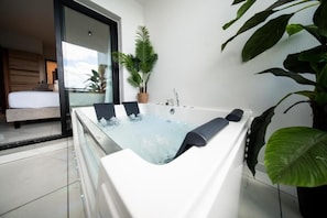 Une salle de bain moderne avec une grande baignoire, une plante en pot et une vue sur une chambre.