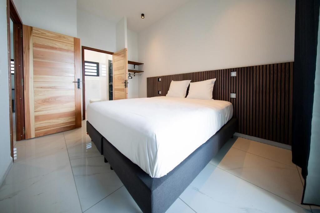 A modern bedroom with a large bed, wooden paneling on the headboard, and a bright, clean design.