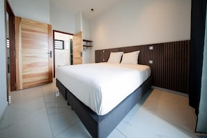 Une chambre à coucher moderne avec un grand lit, un revêtement mural en bois au niveau de la tête de lit et un aménagement lumineux et épuré.