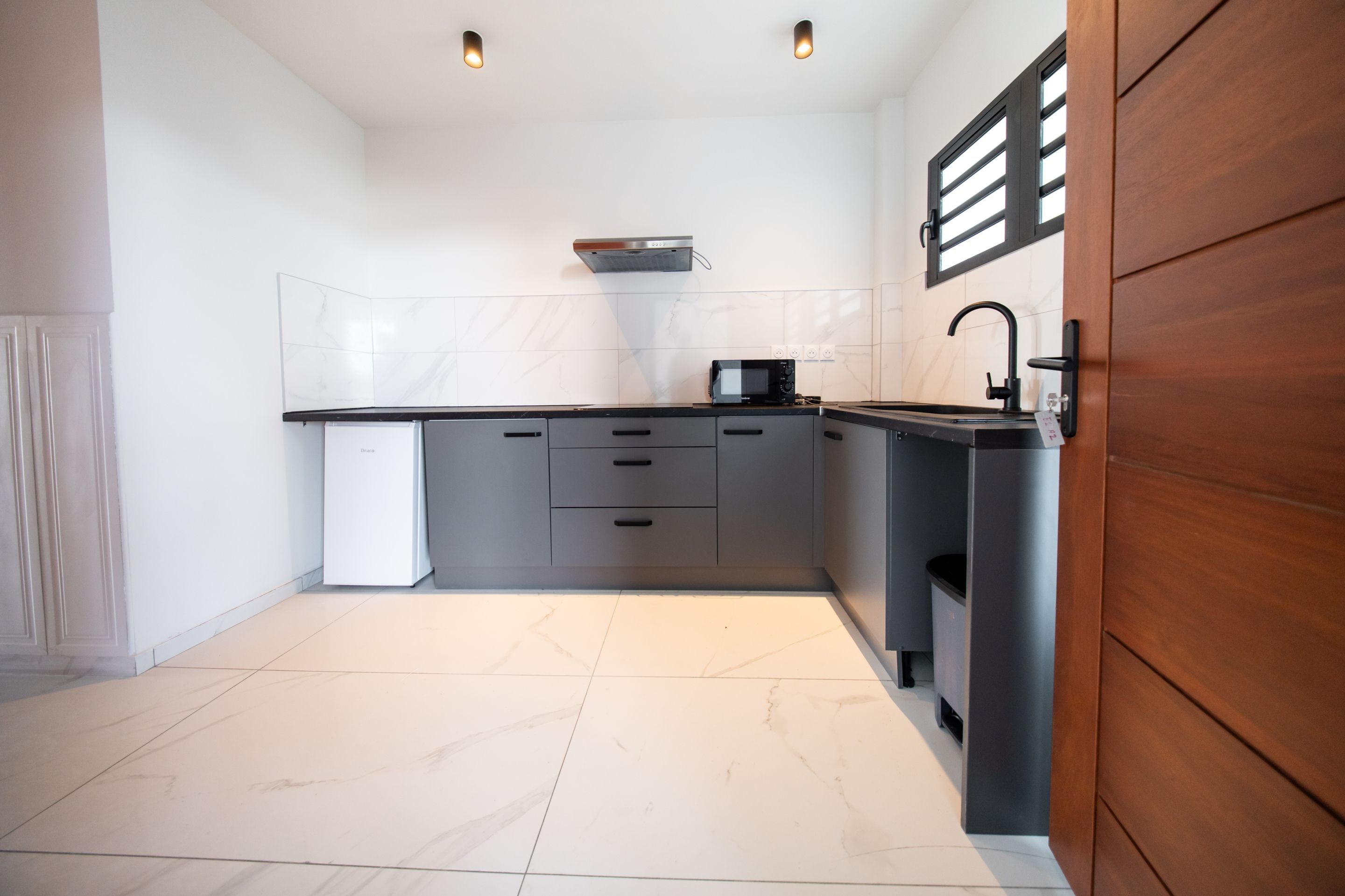 Een moderne keuken met een zwart aanrecht, witte tegels en een houten deur.